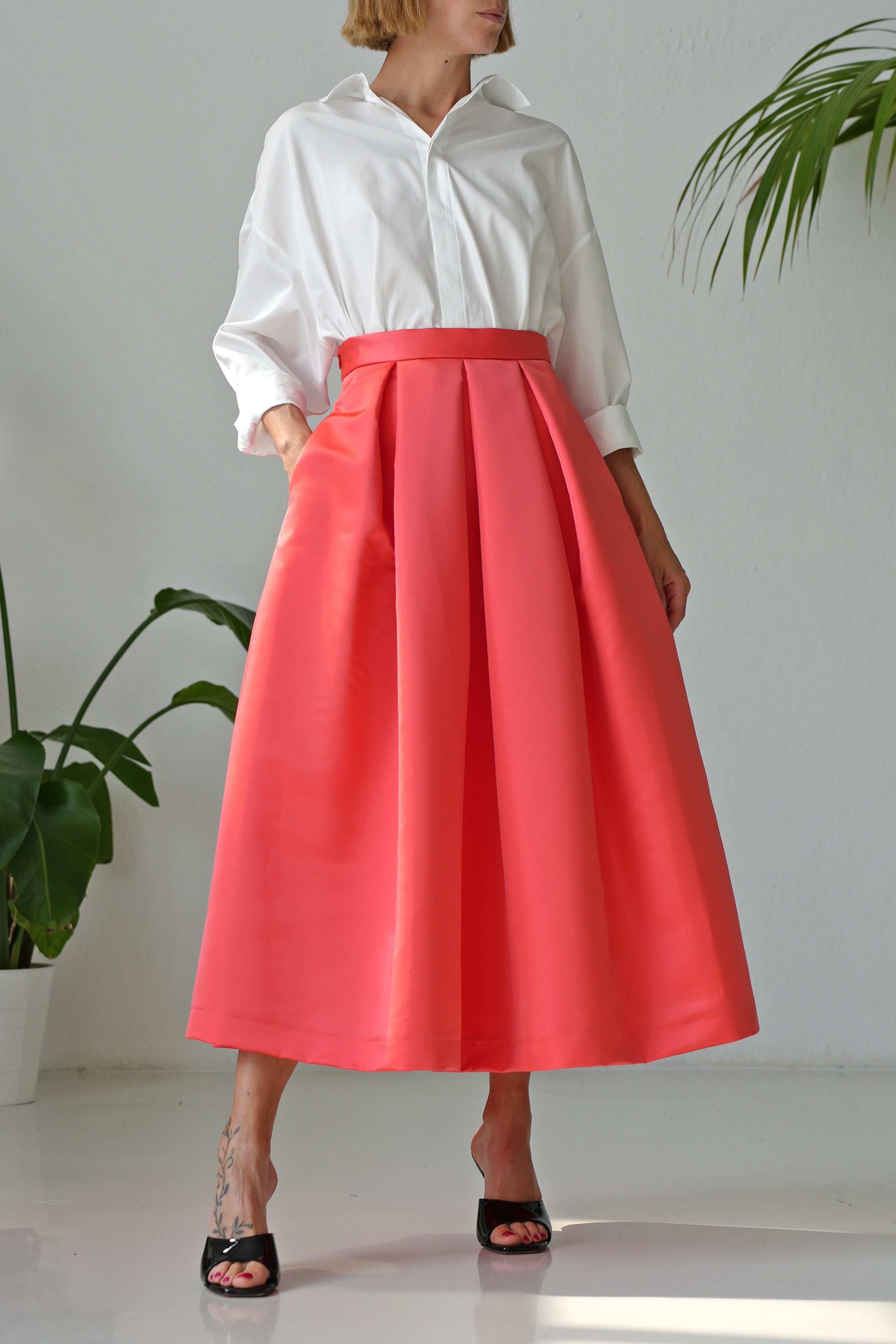 Woman wearing pleated salmon-colored duchesse skirt paired with white blouse and black heels