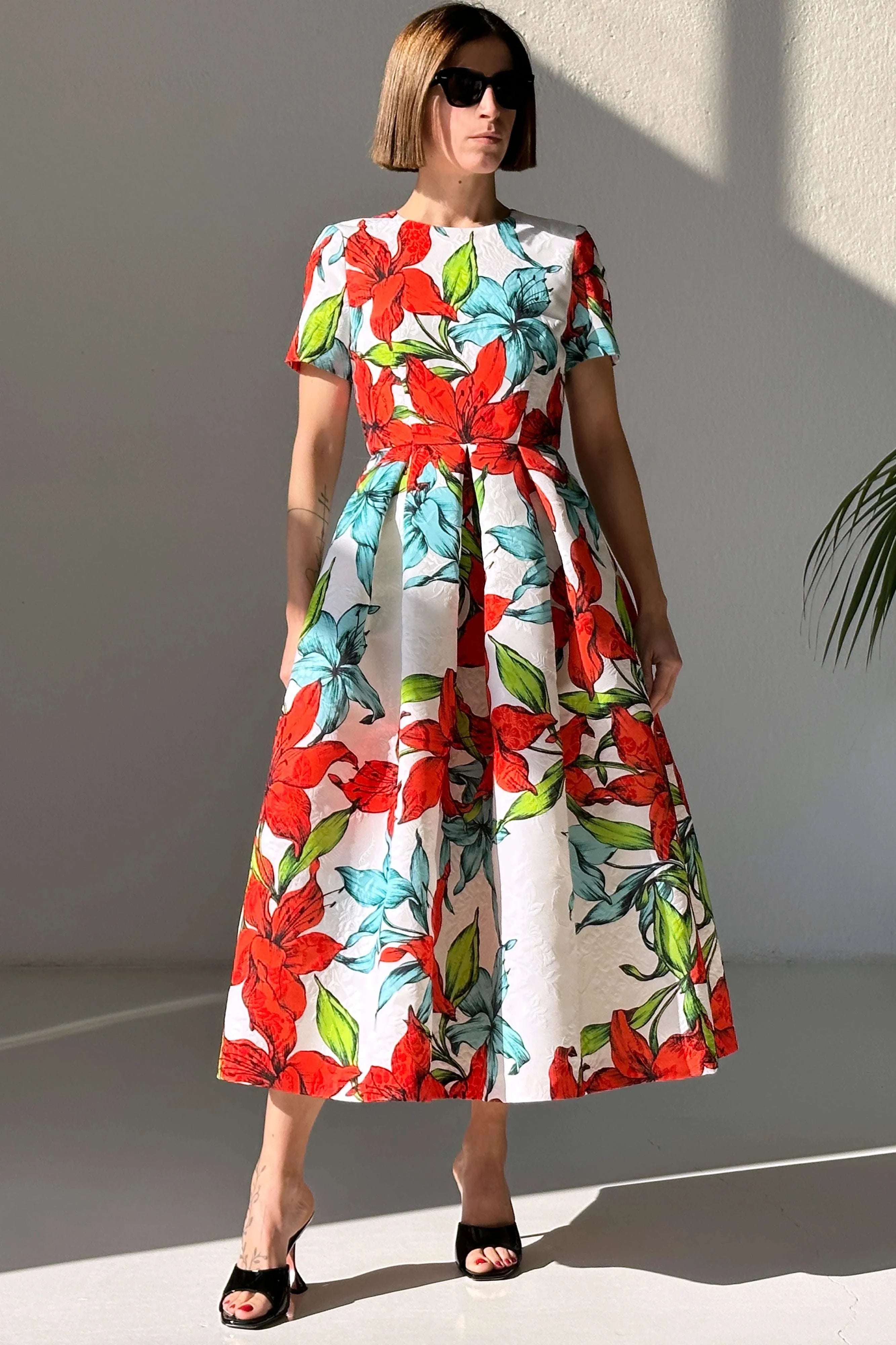 Woman wearing Abito Flower Red Azur dress with red and blue floral print, short sleeves, pleated skirt, and pockets.