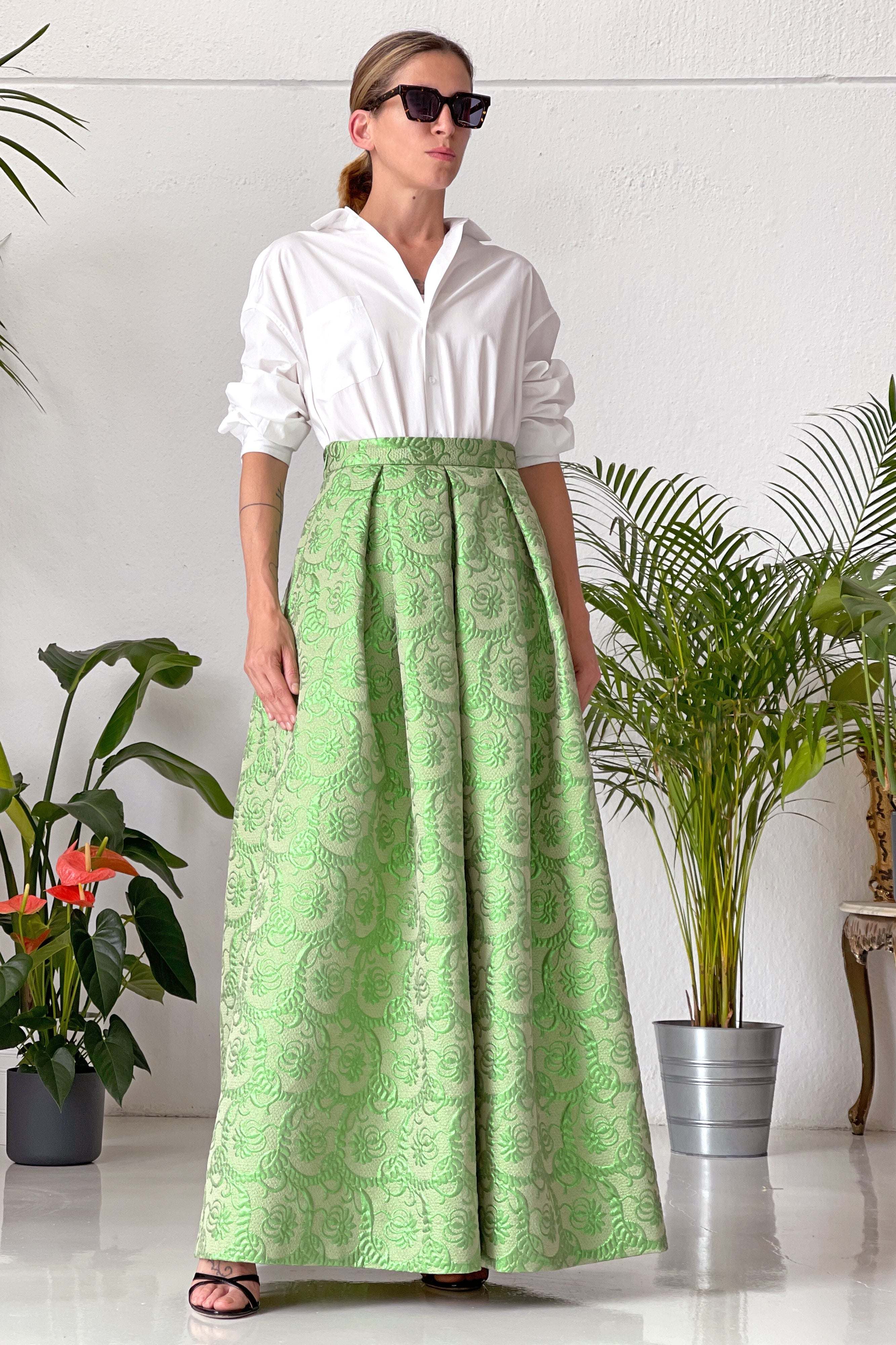 Donna con gonna lunga lurex verde a vita alta e ampia in tessuto jacquard, abbinata a camicia bianca e occhiali da sole neri