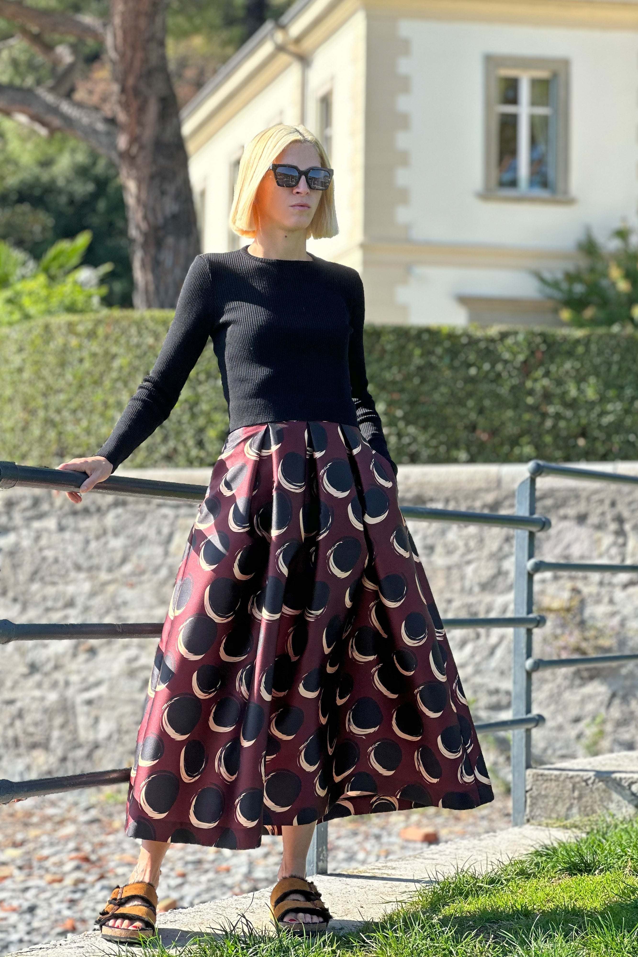 Femme portant une jupe midi taille haute à motifs marron et noir ainsi qu'un haut noir à manches longues à l'extérieur