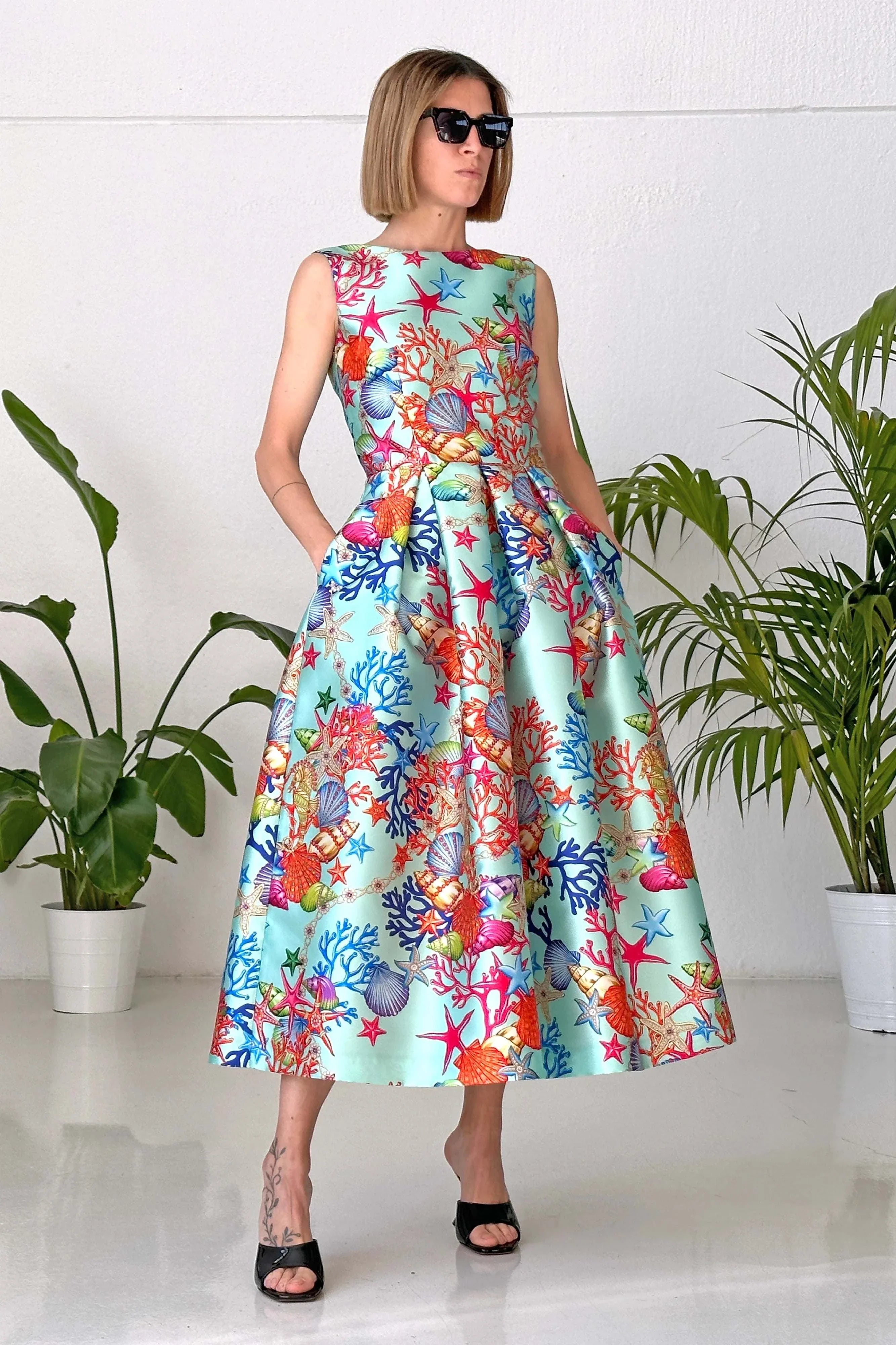 Woman wearing Abito Reef Azur sleeveless pleated mikado dress with colorful reef print and pockets